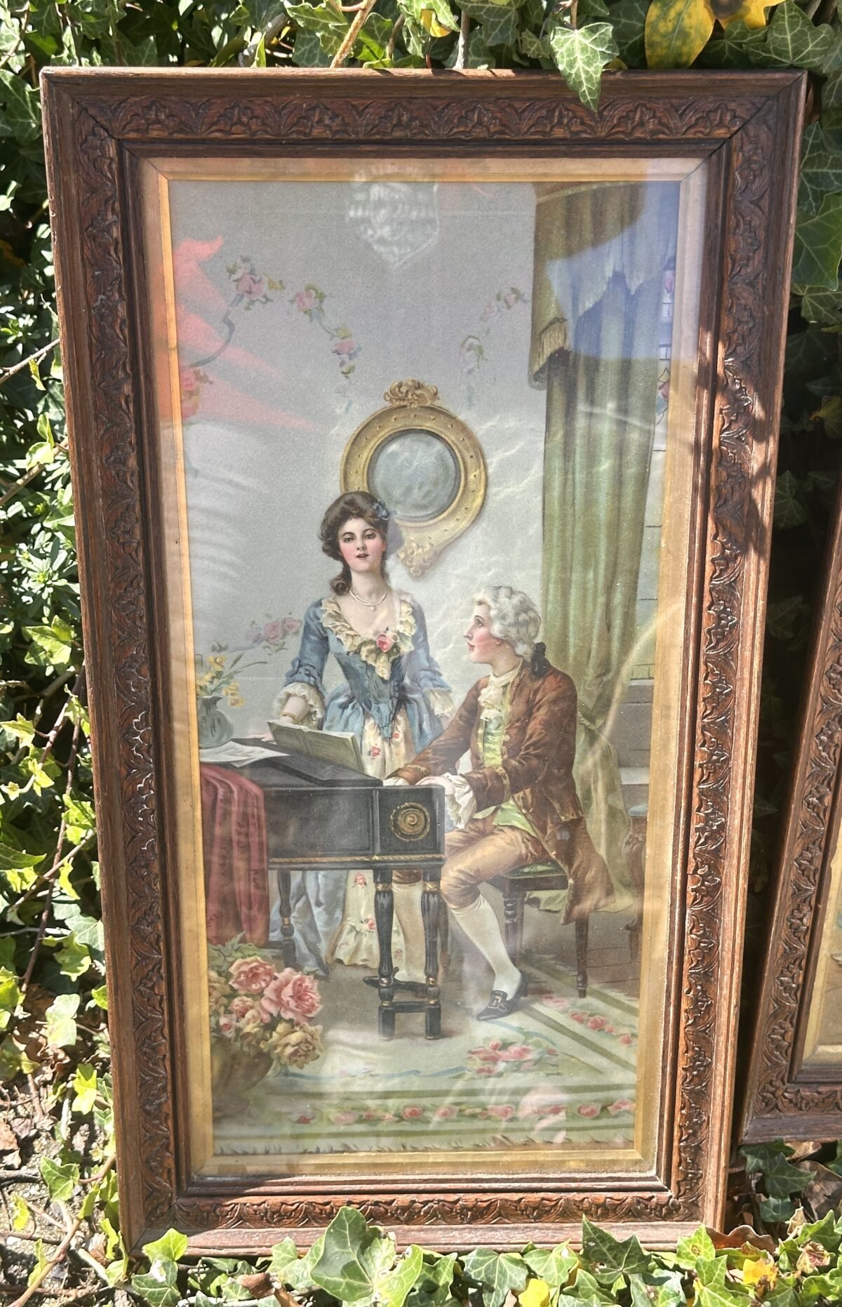 <p>Plaat in oblong houten lijst met afbeelding van een man aan een klavecimbel/piano met dame in blauwe jurk</p> - Brocante