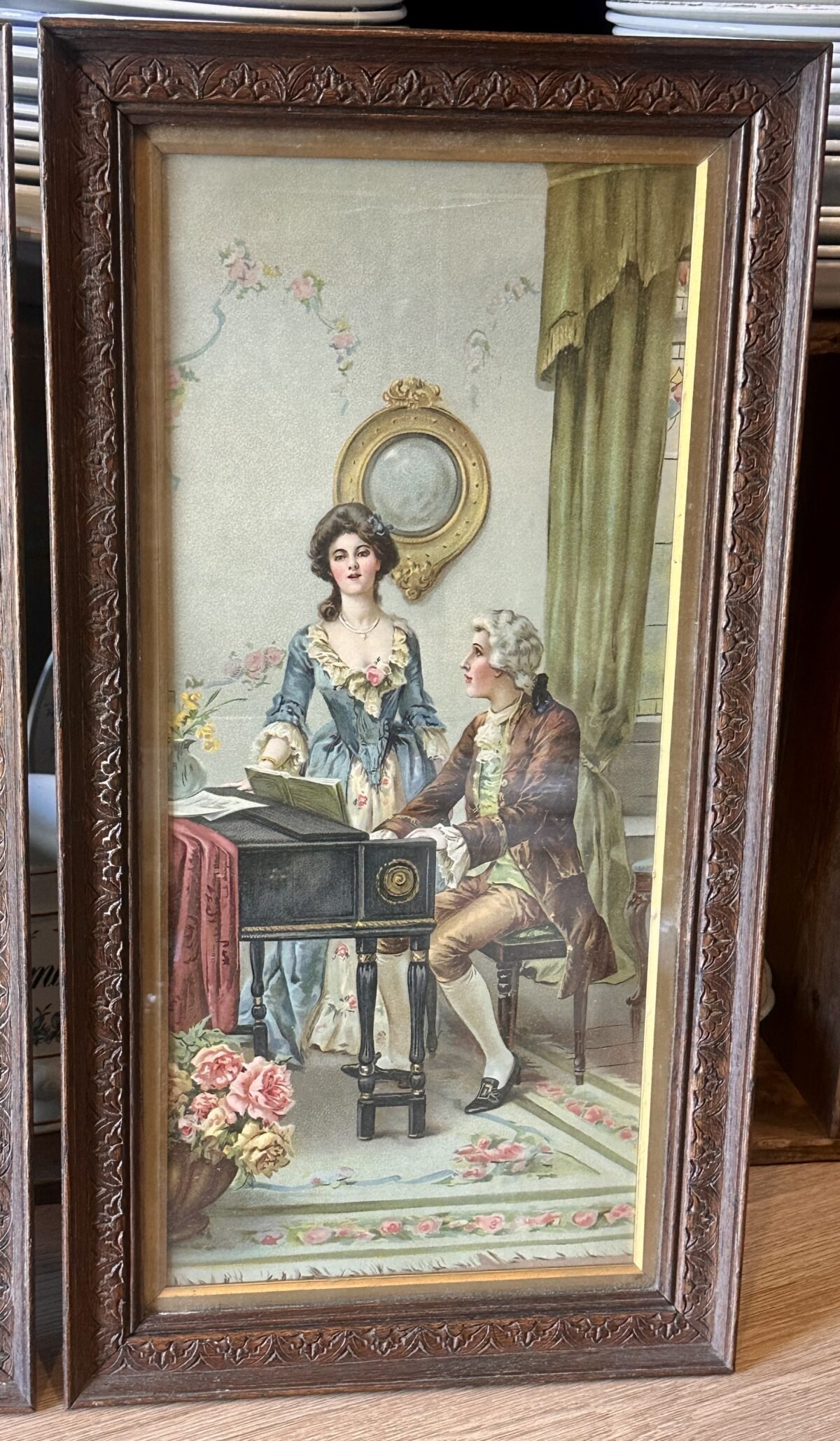 <p>Plaat in oblong houten lijst met afbeelding van een man aan een klavecimbel/piano met dame in blauwe jurk</p> - Brocante