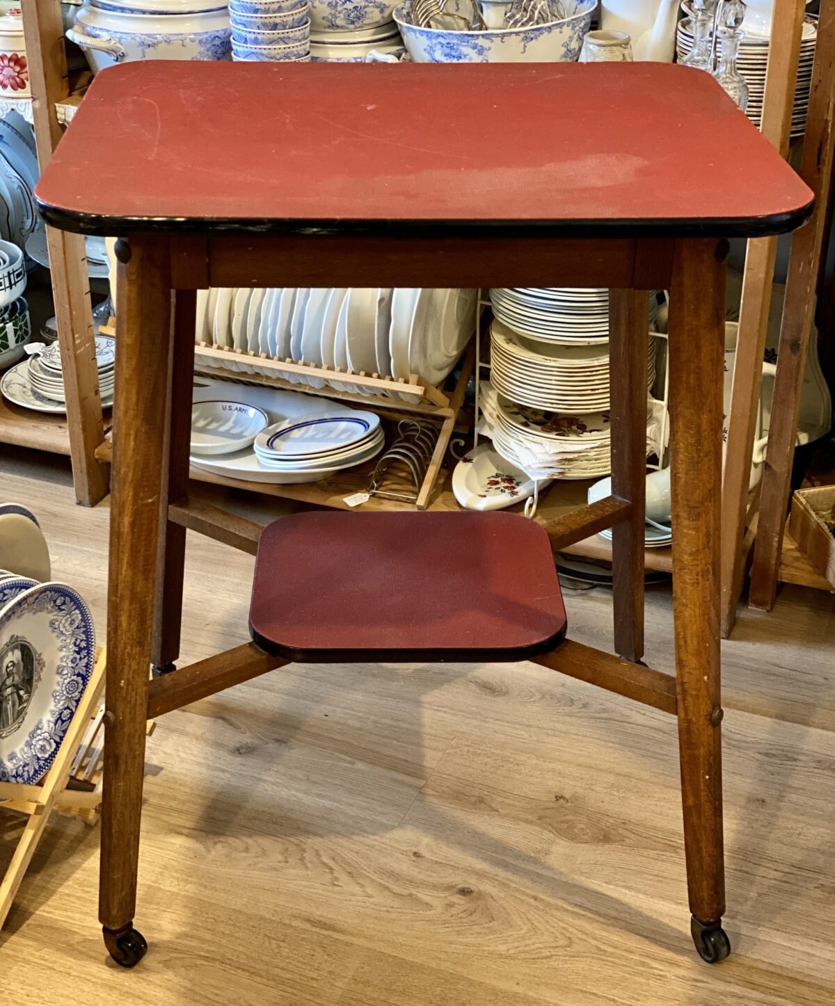 <p>TV-tafel / Bijzettafel op wieltjes - houten poten - donkerrood (skai) blad en extra afzetmogelijkheid onderaan - Vintage</p> - Brocante